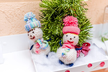 White knitted snowmen in blue and red hats on cotton wool under tinsel Christmas tree. Children's New Year's craft