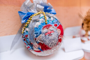 Christmas ball with Santa Claus painted. Ball with white and blue bow and jewelry. Children's craft for New Year