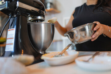 Woman adding sugar to stand mixer while baking in kitchen