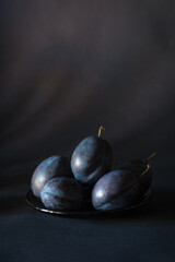 Arrangement with blue purple plums on a background of the same color