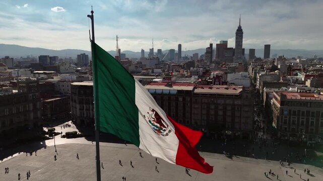 Push-in aerial shot advancing past the Mexican flag toward Torre Latinoamericana at Zocalo square of Mexico City