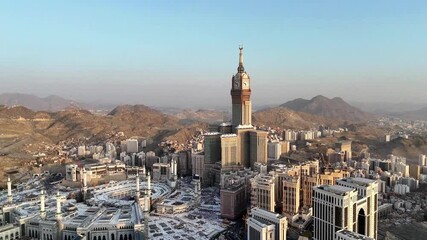 drone footage of Mecca, Saudi Arabia, filmed at sunset. The video captures the vast urban landscape with residential buildings, modern towers, and surrounding mountains bathed in golden hour light - Powered by Adobe