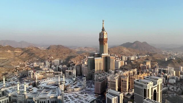 drone footage of Mecca, Saudi Arabia, filmed at sunset. The video captures the vast urban landscape with residential buildings, modern towers, and surrounding mountains bathed in golden hour light