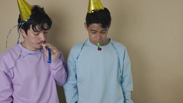 Two Latino youths with party blowers on a light brown background show boredom during a birthday celebration and decide to leave, concept of discouragement, joyless party, and lack of enthusiasm