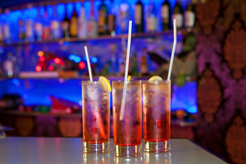 Glasses with cocktails stand on a bar counter against the backdrop of a colorful shelf with drinks