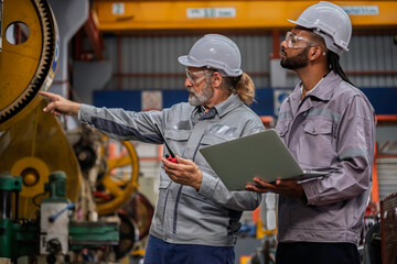 Industrial engineers wearing safety gear inspecting heavy machinery in a modern factory. Factory...