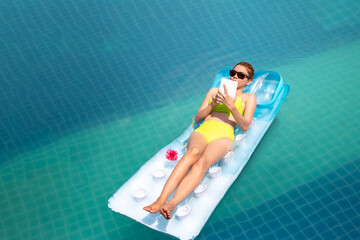 young beautiful woman in bikini enjoy laying in inflamable tube with read on digital tablet and swimming pool in Summer enjoying holidays having sunbath with tan body