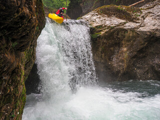 Extreme white water kayaker plunging down a powerful waterfall in a narrow rocky canyon, Austria