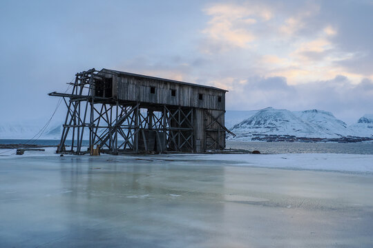 Old wooden structure on icy coast near snow-covered mountains in Svalbard, Arctic Norway, Hiorthamn