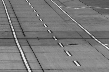 Fototapeta premium A black-and-white view of an airport tarmac road featuring parallel white line markings, emphasizing operational layout under overcast skies. Stock photo