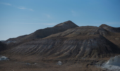 eroded hills with layered sediment formations under a clear blue sky, showcasing the textures and rugged terrain of an arid, rocky desert landscape, highlighting natural geological patterns