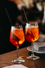 Two Aperol spritz cocktails served in elegant glasses, bar atmosphere, social drinking scene.