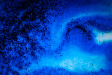 Abstract image in deep blue shades with black specks, resembling an ocean wave, galaxy swirl, or cosmic nebula with flowing textures.