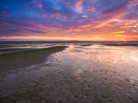 Sunset reflections at Holy Island at low tide Tidal flats reflecting dramatic sunset sky with vibrant clouds and wet sand at low tide