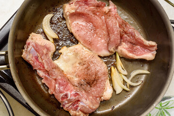 A top view of marinated meat being fried with onions and vegetable oil in a frying pan.