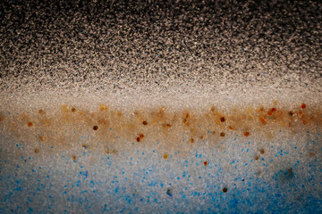 Abstract close-up with a gradient of black, white, orange, and blue specks, resembling a cosmic horizon or sandy texture with scattered particles.