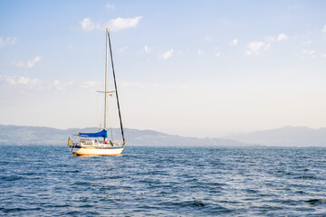 a sailboat illuminated by the sun against the backdrop of a mountainous coastline