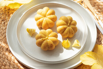 Pumpkin-Shaped Mini Cakes with Cream and Autumn Decor on Woven Placemat
