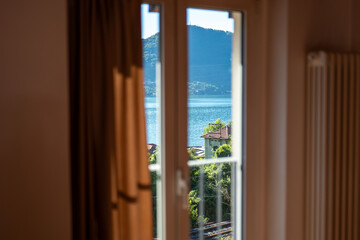 Fototapeta premium Scenic view of a tranquil lake framed by curtains from a cozy room, showcasing mountains and nature during daylight