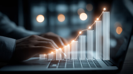 Rising bar chart projected from a laptop while hands type, illustrating business growth driven by digital strategy and performance optimization.
