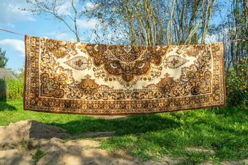 Machine made carpet hanging outdoors on clothesline in rural area. Synthetic decorative carpet drying in open air with geometric design and neutral colors in natural setting.