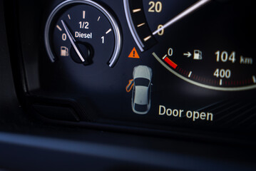 Close up view of a BMW X6 instrument cluster showing a fuel gauge, speedometer, and digital display with a door open warning and 104 km range.