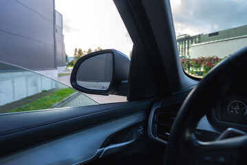 Naklejka premium Interior view of a BMW X6 showing the driver's side mirror, dashboard details, and a reflection of an outdoor scene with buildings and greenery.