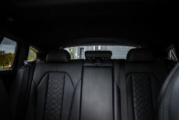 Naklejka premium Close up of BMW X4 rear seats with black leather, hexagonal quilting, visible headrests, and a folded armrest. Modern building seen through rear window.