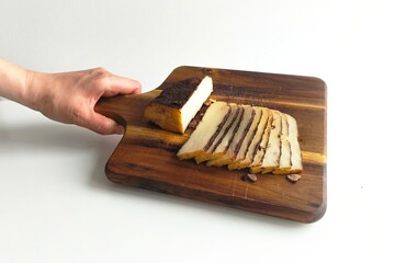 Hand holding a rustic wooden board with neatly sliced smoked cheese, showcasing traditional dairy snack and natural food presentation.