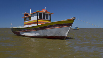 Naklejka premium Old fishing boat in the middle of the river with beautiful sunny blue sky and sea in the background.