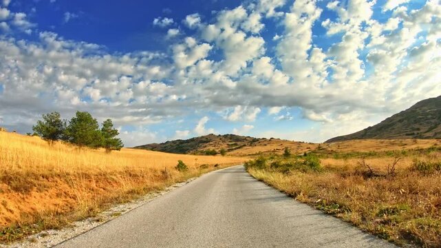 Amazing nature, fluffy clouds blue sky, dry meadows, golden hour, POV drive