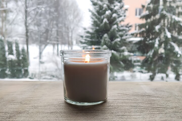 A candle in glass jar glowing on winter window sill.