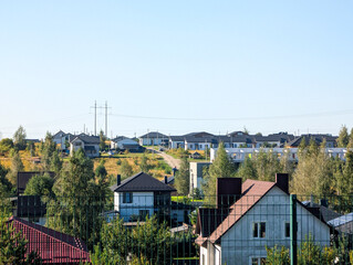 Bright summer afternoon view of a modern, organized suburban neighborhood with rows of detached houses and power lines stretching across a gently rising grassy hill under a clear, bright blue sky.