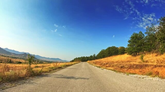 Beautiful blue sky, golden slopes, evergreen grove, distant mountains, POV drive
