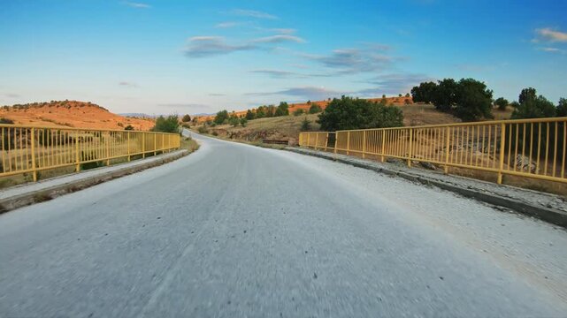 POV car driving on local road, hills, golden slopes, scattered trees, blue sky