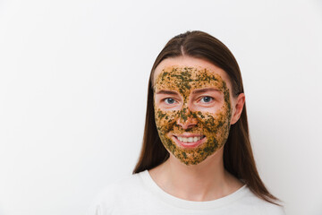 Portrait of young girl or woman with green natural homemade cosmetic mask on her face with white background. Concept of self-care at home or in salon. Copy space