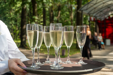 A waiter holds a tray of champagne. Many glasses of champagne are on the tray.