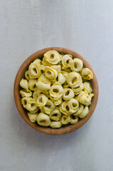 Raw homemade tortellini in a wooden bowl on a gray background. Traditional Italian food concept. Selective focus. Vertical orientation. Top view.