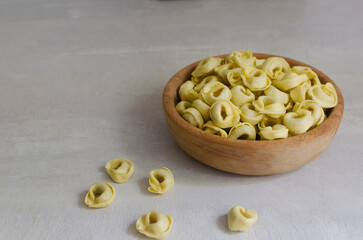 Raw homemade tortellini in a wooden bowl on a gray background. Traditional Italian food concept. Selective focus. Horizontal orientation. Copy space