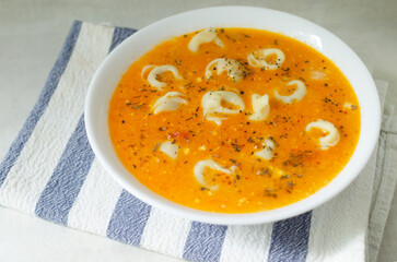 Tortellini soup with chicken and parmesan in a white bowl on a striped napkin on a gray background. Traditional Italian food concept. Selective focus. Horizontal orientation.