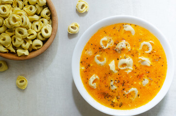 Tortellini soup with chicken and parmesan in a white bowl on a gray background. Traditional Italian food concept. Selective focus. Horizontal orientation. Top view.