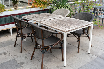 An empty street cafe or restaurant terrace with gray wooden tables and wicker chairs surrounded by greenery, no people.