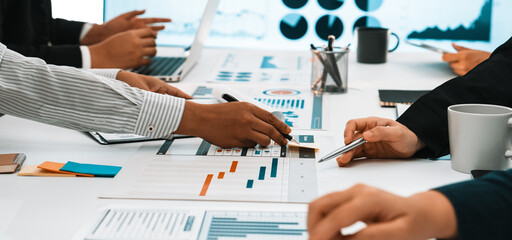 A diverse business team engages in active collaboration at a modern office setting. They analyze charts and graphs while discussing strategies over laptops and documents. SACTR