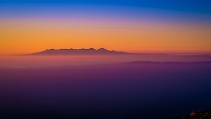 Fototapeta premium Dramatic mountain range silhouette at sunset with vibrant colors and hazy atmosphere