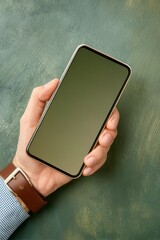 A man's hand holds a modern smartphone with a blank screen against a dark green background