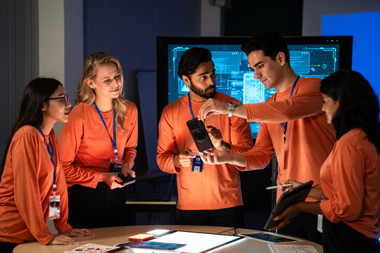 A team of engineers and UI UX designers collaborates on a smartphone prototype, They examine the device ergonomics and operate the mobile interface user flow, product innovation during a design review