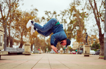 Young man doing an acrobatic flip with incredible agility and balance on city pavement