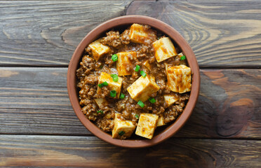 Mapo tofu dish with tofu in spicy sauce with minced beef in a ceramic bowl on a wooden background. Dish from Sichuan province. Traditional Asian food concept. Selective focus. Top view.