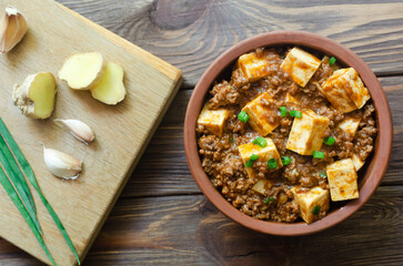 Mapo tofu dish in spicy sauce with minced beef in a ceramic bowl on a wooden background. Dish from Sichuan province. Traditional Asian food concept. Selective focus. Horizontal orientation. Top view.