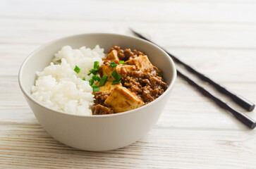 Mapo tofu dish in spicy sauce with minced beef in a ceramic bowl on a white background. Dish from Sichuan province. Traditional Asian food concept. Selective focus. Horizontal orientation.